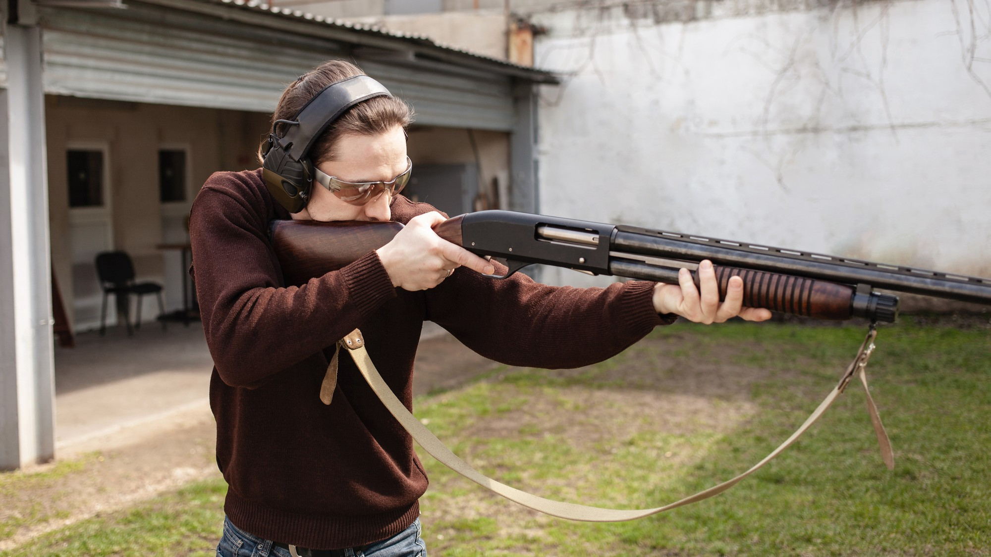 man protective glasses headphones holding pump action shotgun